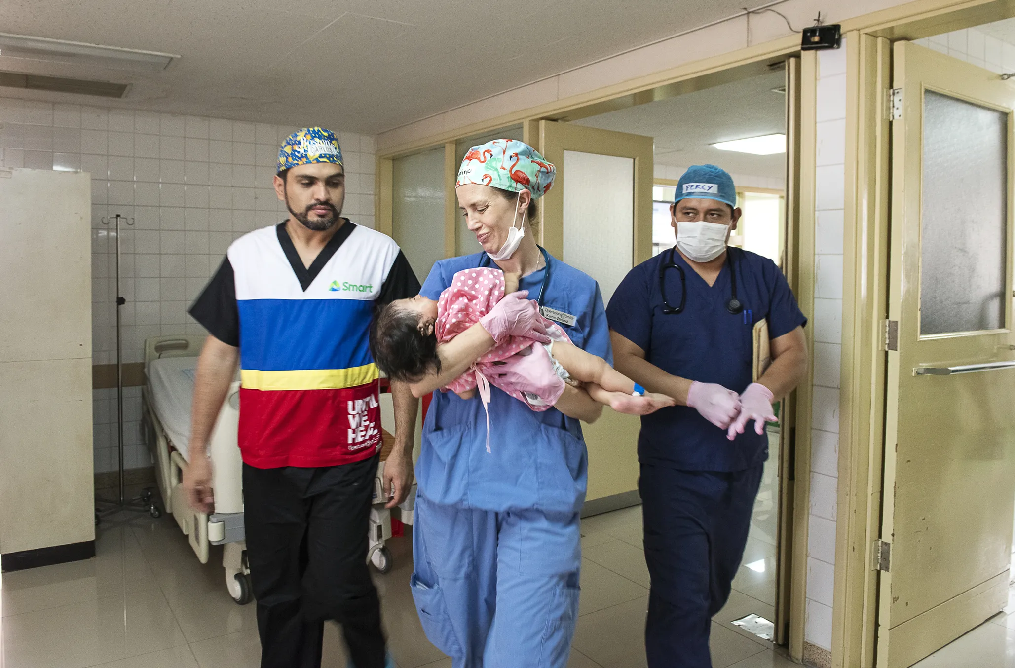 Volunteer cleft surgeon Dr. Carlos Hugo Dorado of Bolivia, left, and pediatric anesthesiologist Dr. Karin Strand of Sweden, center, carry Heydi out of the operating room toward the waiting arms of her grandmother, Claudina.