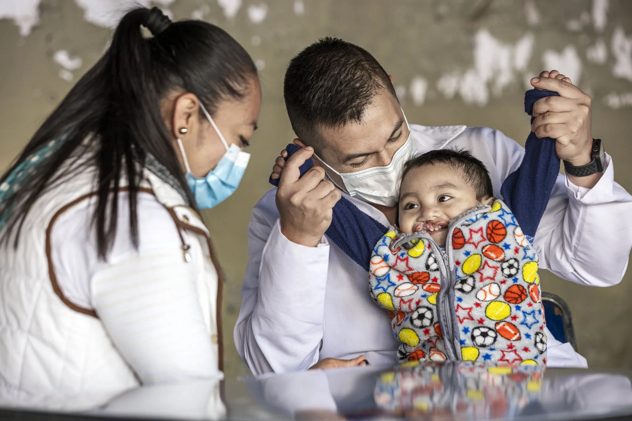 Sebastian smiles wide while in the arms of an Operation Smile volunteer nurse. His mother, María, sits beside them during screening at a 2021 surgical program.