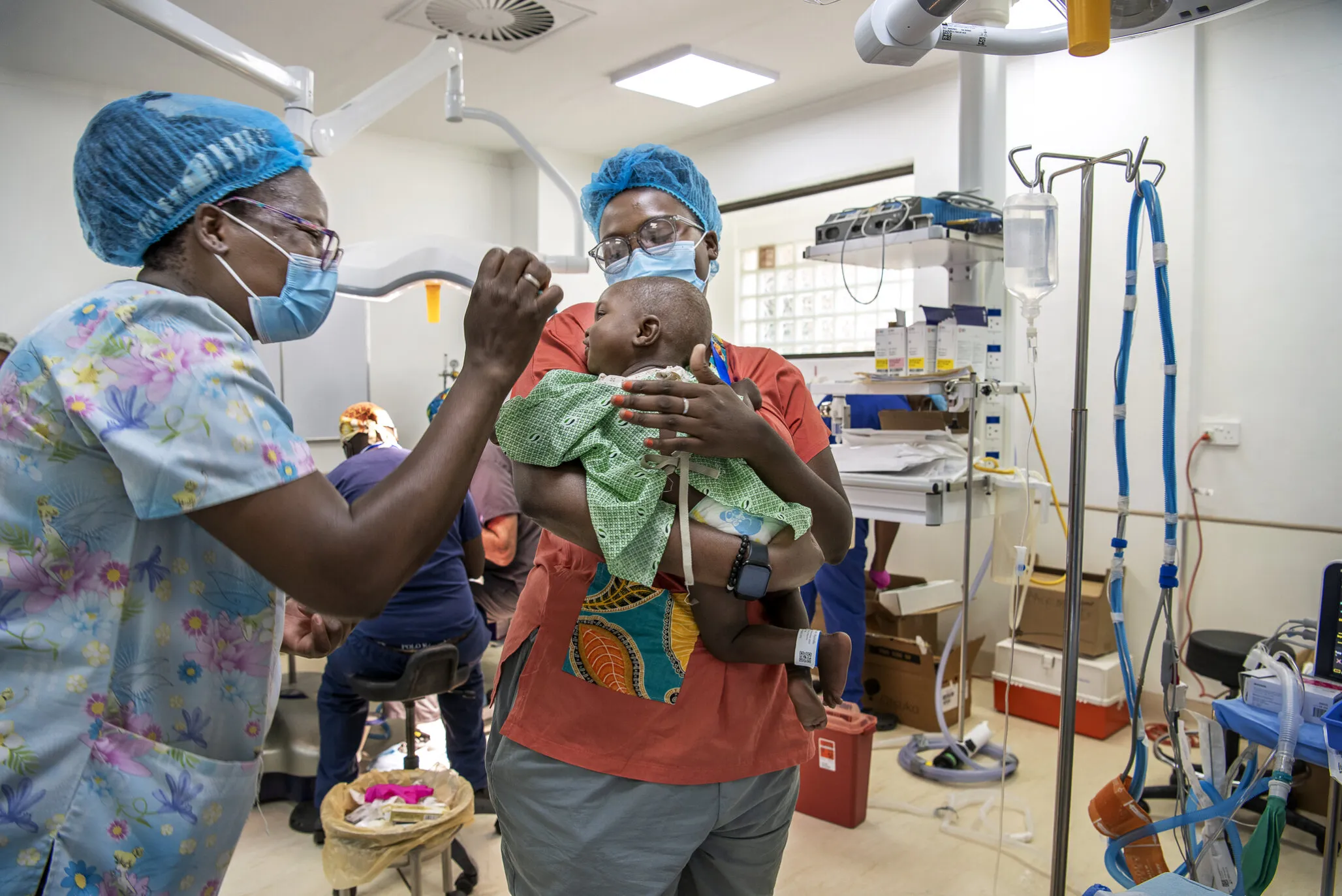 While inside the operating room with 1-year-old Tumpale, psychosocial care providers Cathy Cheonga and Faith Cheonga of Malawi comfort him prior to surgery.
