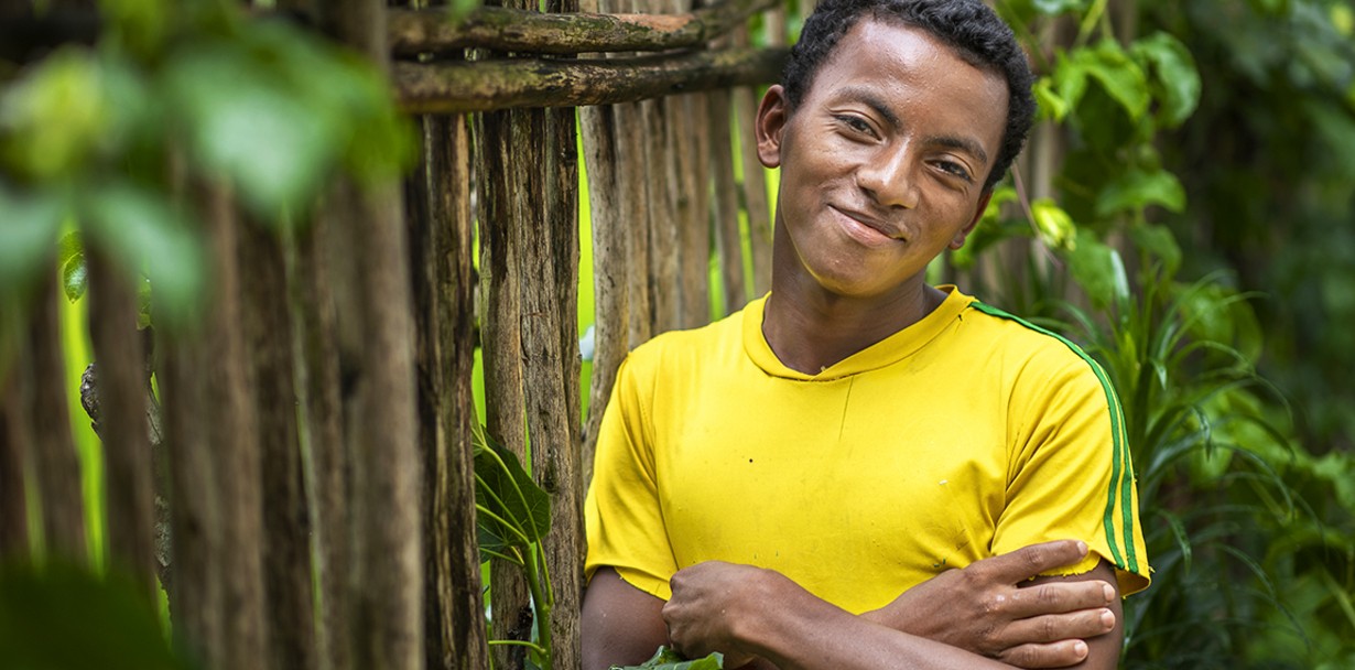 Herve poses in a yellow short sleeve shirt beside a wooden fence to show everyone his new smile.