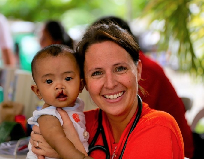 Stacie Goodrich, registered nurse at Intermountain Healthcare in Salt Lake City and Operation Smile volunteer, poses with a young patient from the Philippines during a 2016 surgical program. Stacie is wearing a red T-shirt and smiling while holding the young patient. 