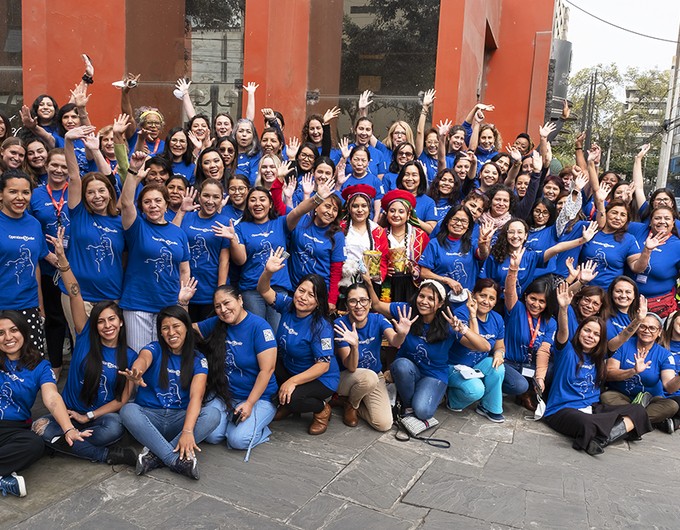 Dozens of female medical volunteers attending the Lima, Peru, Women in Medicine surgical program pose for a group photo. The women are wearing blue shirts and raising their hands in celebration.