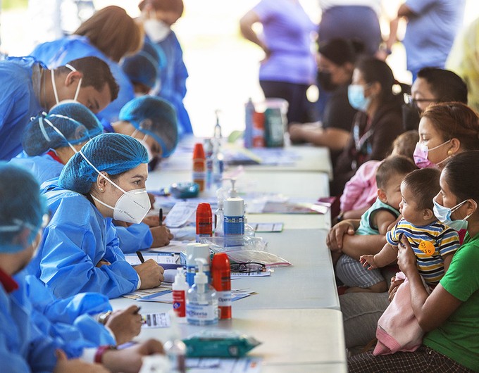 On one side of the screening table, volunteers dressed in blue personal protective equipment. On the other, patients and families answer questions and provide information about their journey to the surgical program in Honduras.