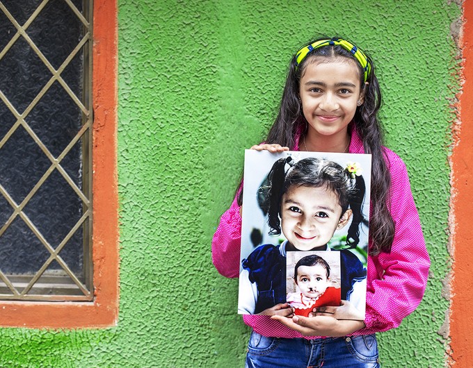 Thirteen-year-old Laura from Colombia stands in front of a green wall holding both of her "before" images.