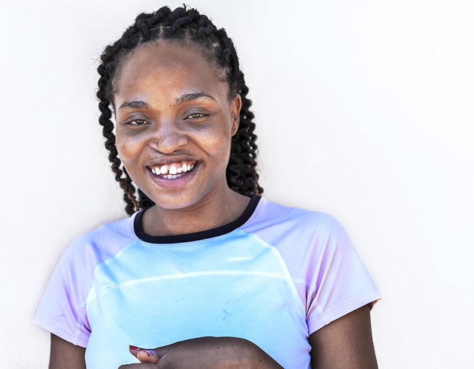 Standing in front of a white wall, nonmedical volunteer and Operation Smile patient Carol Chigona smile wide for the camera.