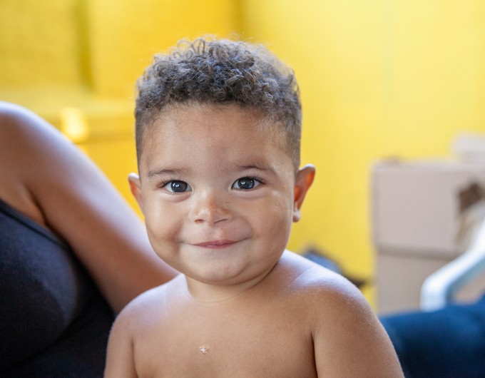 One-year-old Wesilyn smiles wide months after receiving cleft surgery. Behind him is a bright yellow wall.