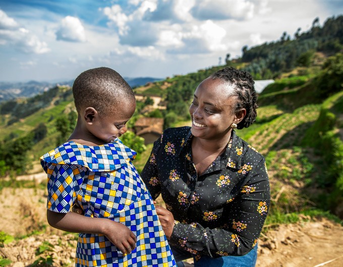Dr. Françoise Mukagaju, the first female plastic surgeon in Rwanda, stands beside Valentine, a young patient who received surgery during an Operation Smile surgical program. Valentine wears a blue and yellow dress while Françoise wears a black shirt with yellow flowers.  