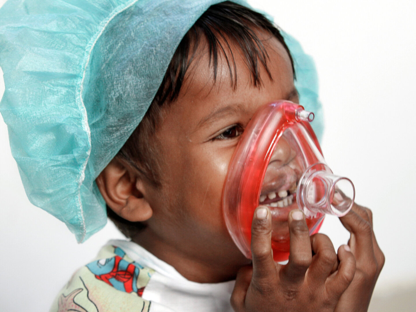 Sarban, 5 years old, wears a scrub cap and plays with a toy anesthesia mask over to help him become more comfortable with the medical equipment he will likely see after entering the operating room for his surgery