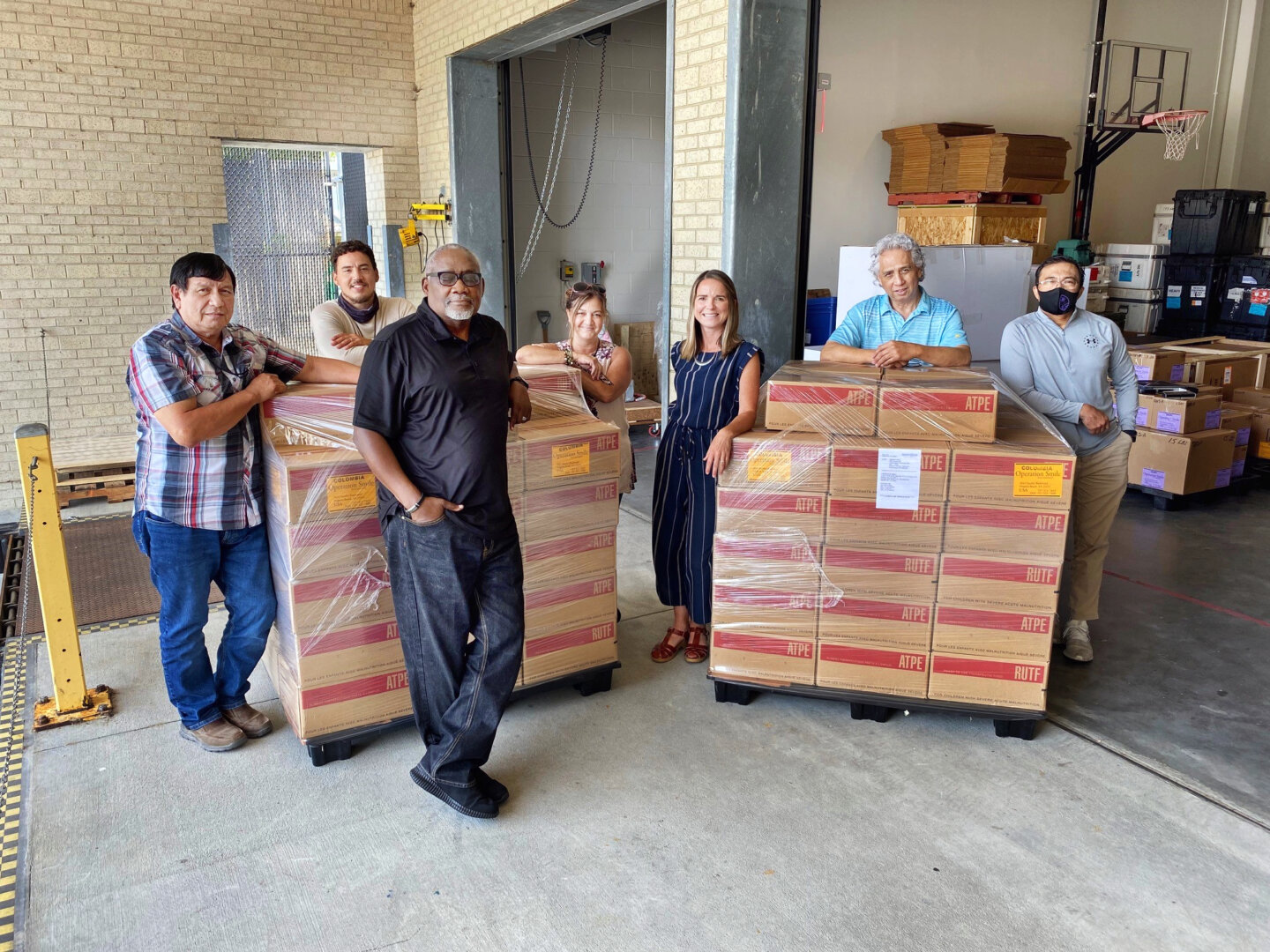 Members of the Operation Smile logistics team pose for a photo with the historic shipment of RUTF before its forwarding to Colombia in May 2021. Pictured are, from left: Joe Sanchez, pharmacy specialist; Chris Brewington, warehouse assistant; Jesse Hines, chief of logistics and facilities; Yolanda Weaver, logistics quality assurance coordinator; Candace Streit, director of logistics; Edd Basilio, warehouse specialist; and Jojo Ocampo, warehouse team lead.