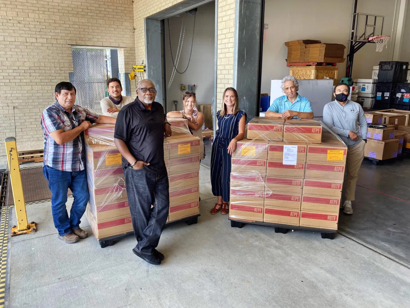 Members of the Operation Smile logistics team pose for a photo with the historic shipment of RUTF before its forwarding to Colombia in May 2021. Pictured are, from left: Joe Sanchez, pharmacy specialist; Chris Brewington, warehouse assistant; Jesse Hines, chief of logistics and facilities; Yolanda Weaver, logistics quality assurance coordinator; Candace Streit, director of logistics; Edd Basilio, warehouse specialist; and Jojo Ocampo, warehouse team lead.
