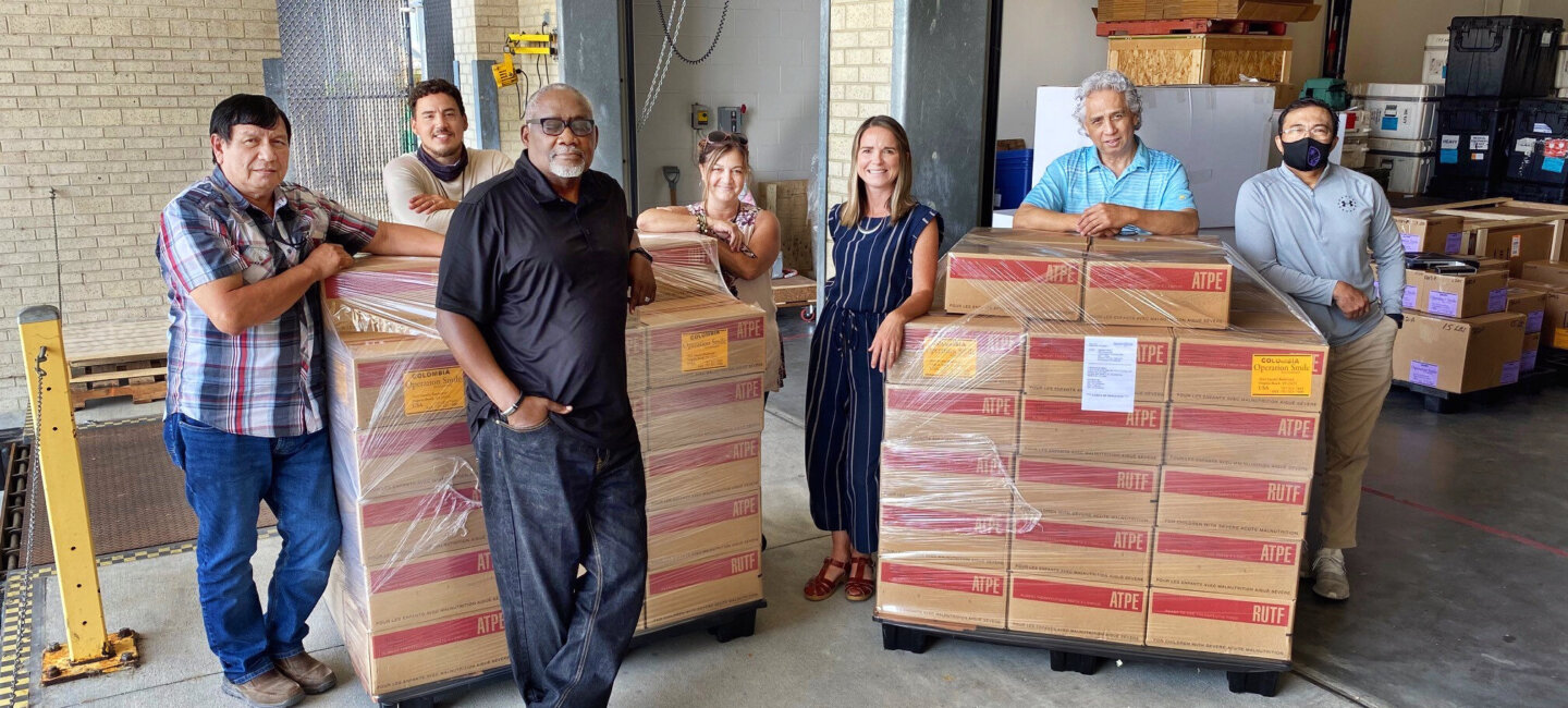 Members of the Operation Smile logistics team pose for a photo with the historic shipment of RUTF before its forwarding to Colombia in May 2021. Pictured are, from left: Joe Sanchez, pharmacy specialist; Chris Brewington, warehouse assistant; Jesse Hines, chief of logistics and facilities; Yolanda Weaver, logistics quality assurance coordinator; Candace Streit, director of logistics; Edd Basilio, warehouse specialist; and Jojo Ocampo, warehouse team lead.