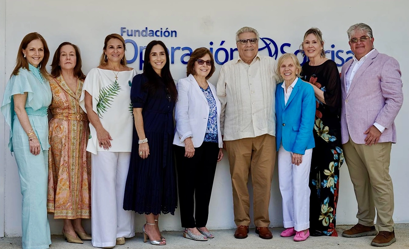 A group of individuals from the United States and Panama wearing colorful formal clothing pose for a group photo in front of a backdrop that has the Operation Smile logo in Spanish.