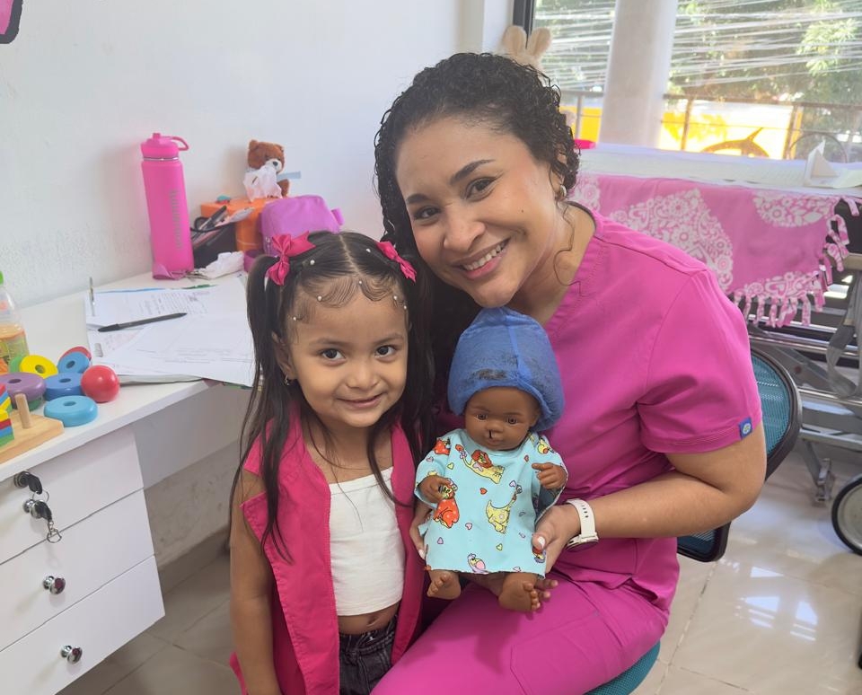 A patient and volunteer smile with a cleft doll.