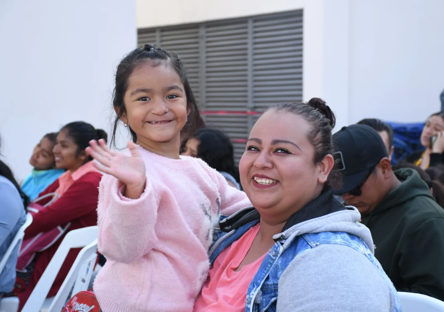 Li waves to the camera, while her mom, Valeria, holds her.
