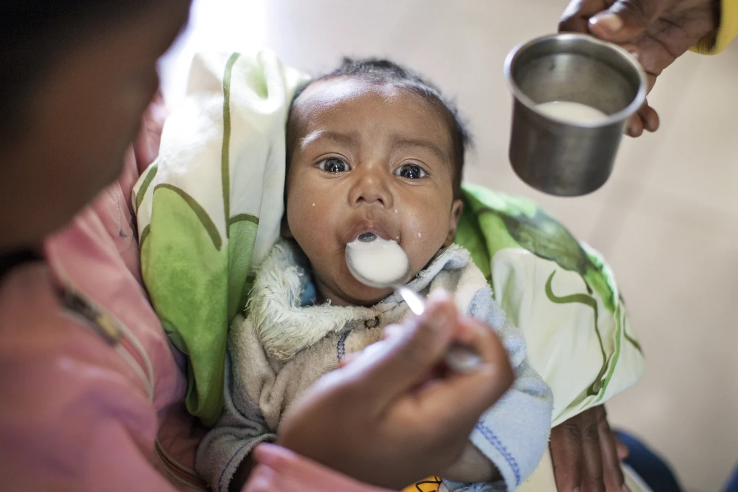 A mother learns how to feed her baby with a spoon during a nutrition program.
