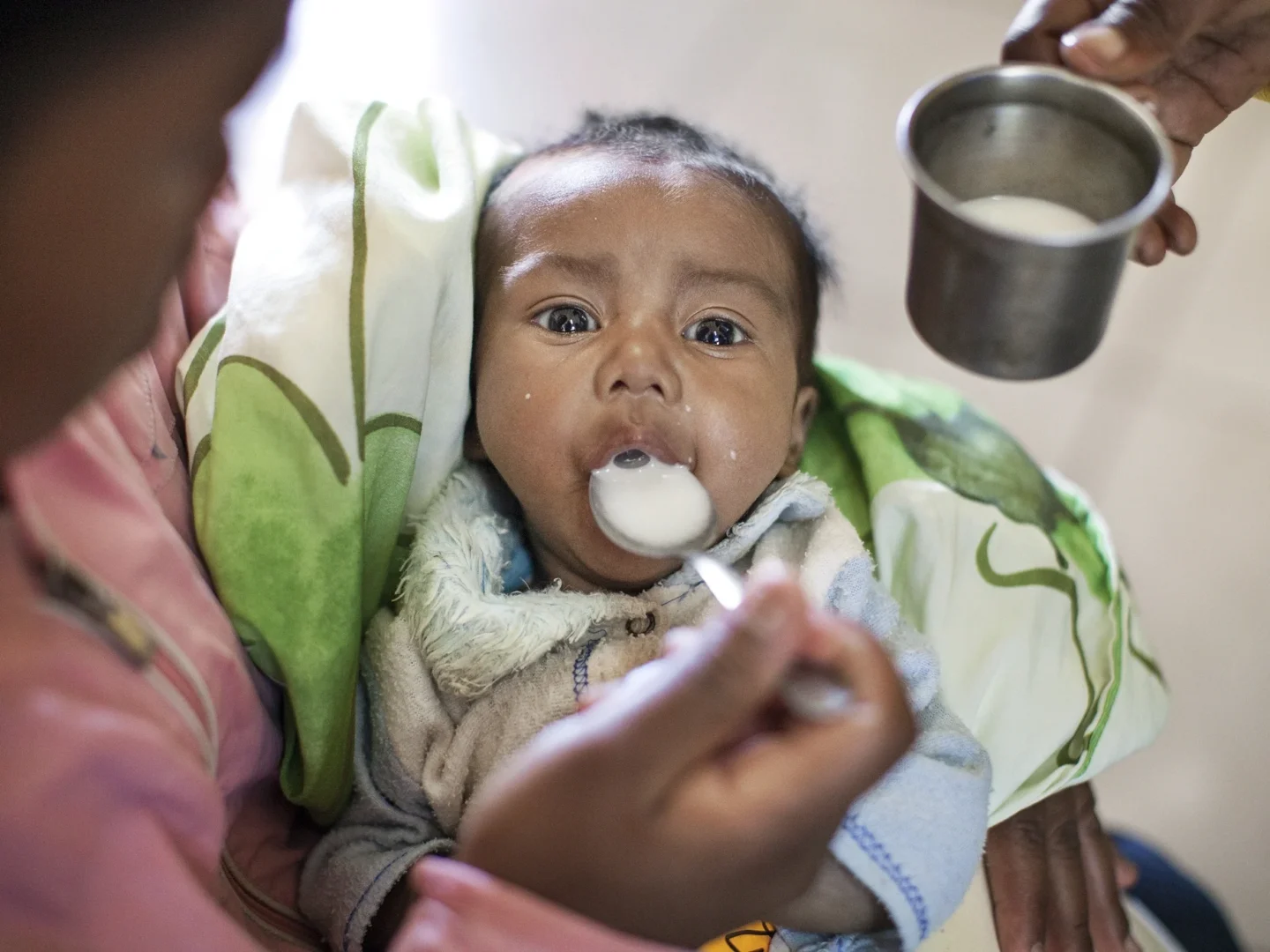 A mother learns how to feed her baby with a spoon during a nutrition program.
