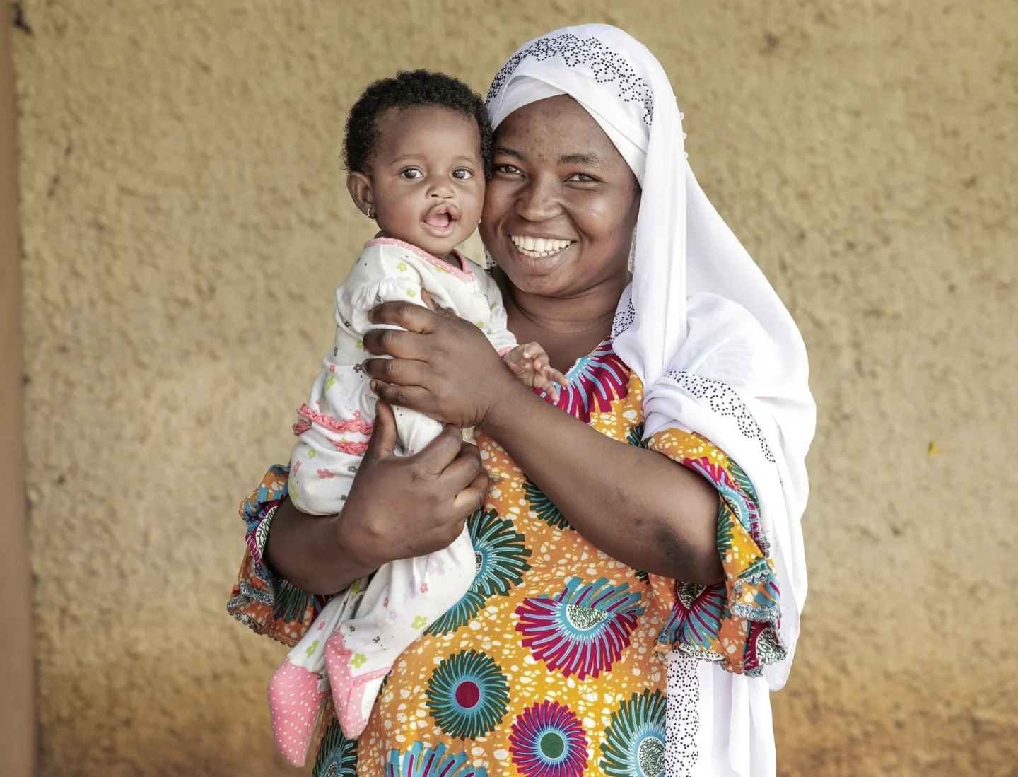 Alimatu smiling and facing the camera while holding her infant daughter Farida, prior to Farida's surgery.