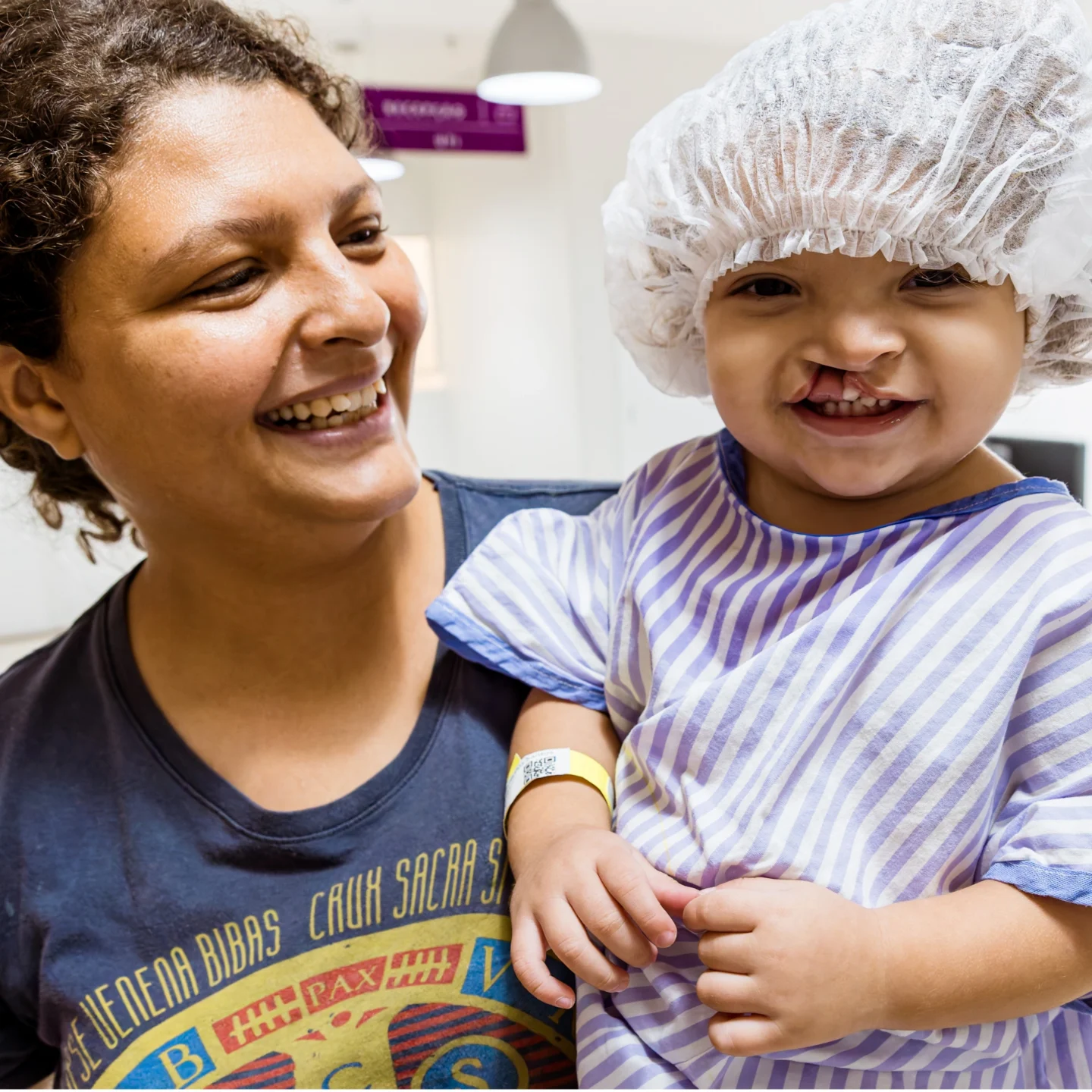 Erica smiles while holding Isis in a white hairnet and striped shirt; both look toward the camera in a brightly lit hospital hallway.