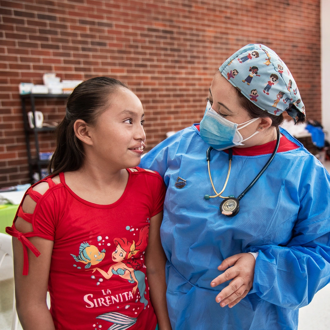 Dayana, a child from Guatemala, chats with an Operation Smile medical practitioner in blue surgical scrubs.